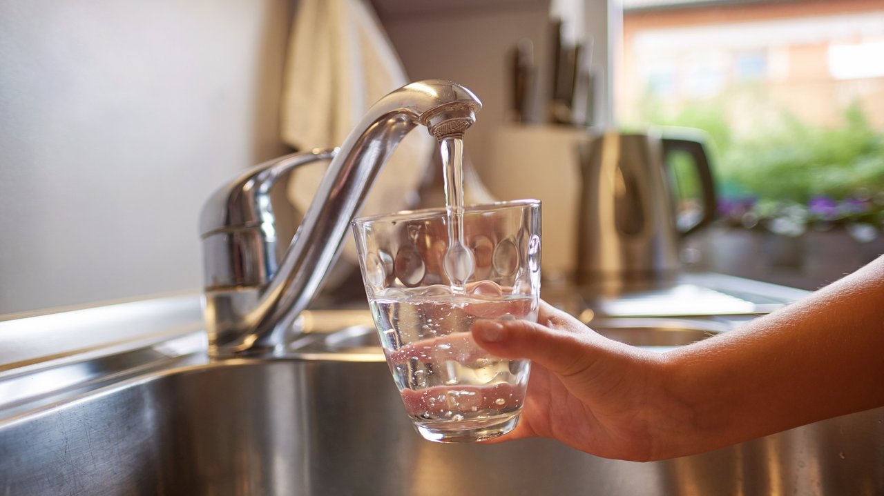 Kinderhand, die sich am Wasserhahn frisches Wasser in ein Glas gießt