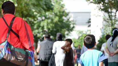 Flüchtlinge gehen am 04.08.2014 in der Landeserstaufnahme für Asylbewerber (LEA) in Karlsruhe (Baden-Württemberg) einen Weg entlang.