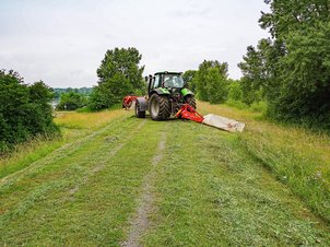 Mäharbeiten mit Scheibenmähwerk an einem Traktor auf einem Damm